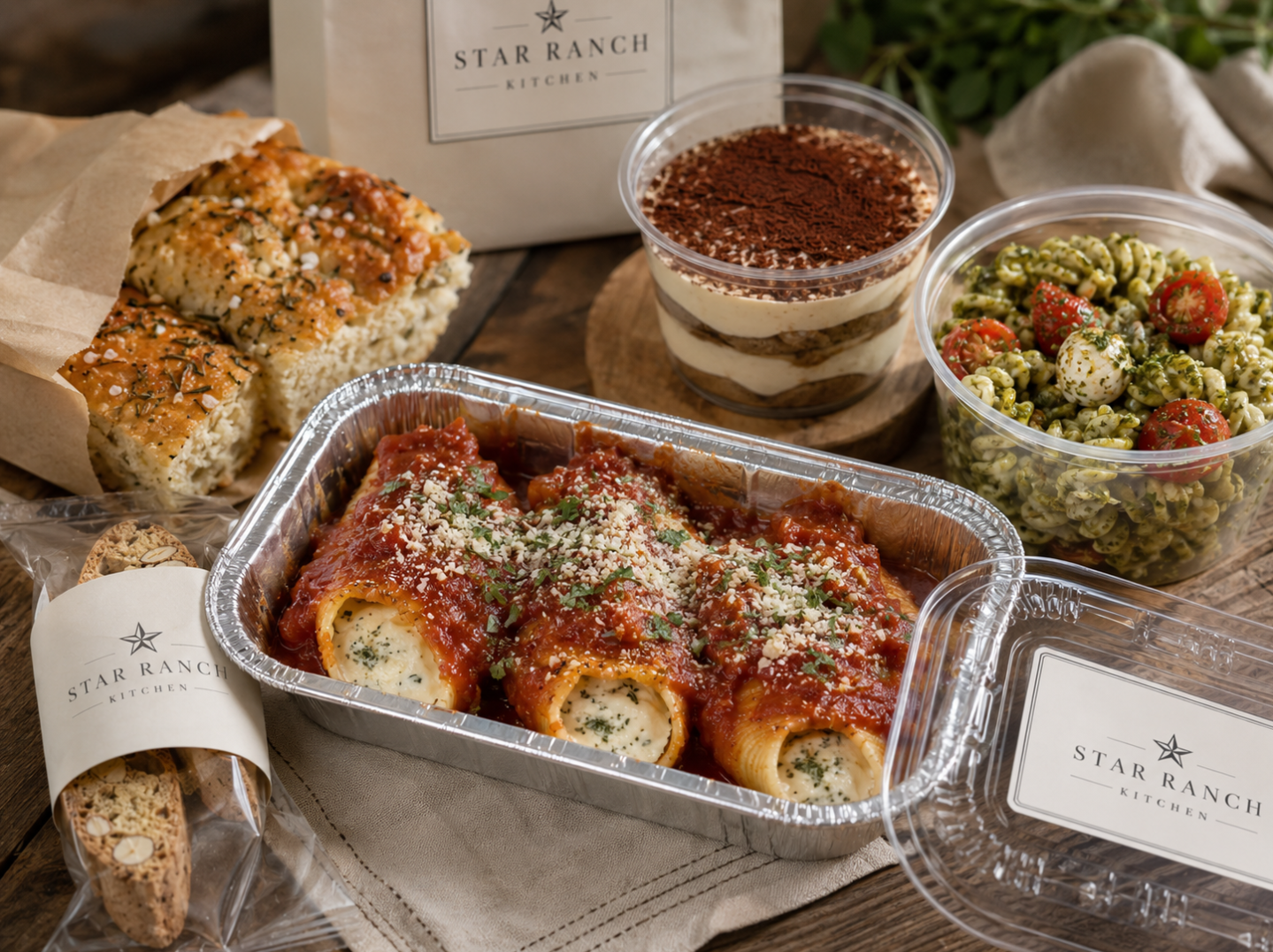 Italian Comfort Plate from Star Ranch Kitchen with cheese-stuffed shells, pesto pasta salad, wood-fired rosemary focaccia, tiramisu cup, and almond biscotti packaged for pickup.